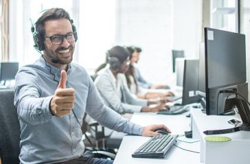 Cheerful male customer service operator showing thumbs up in office.